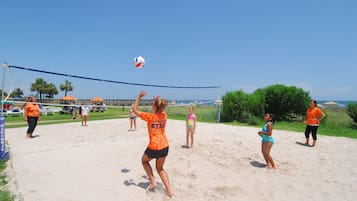 A beach volleyball game with players in orange shirts.