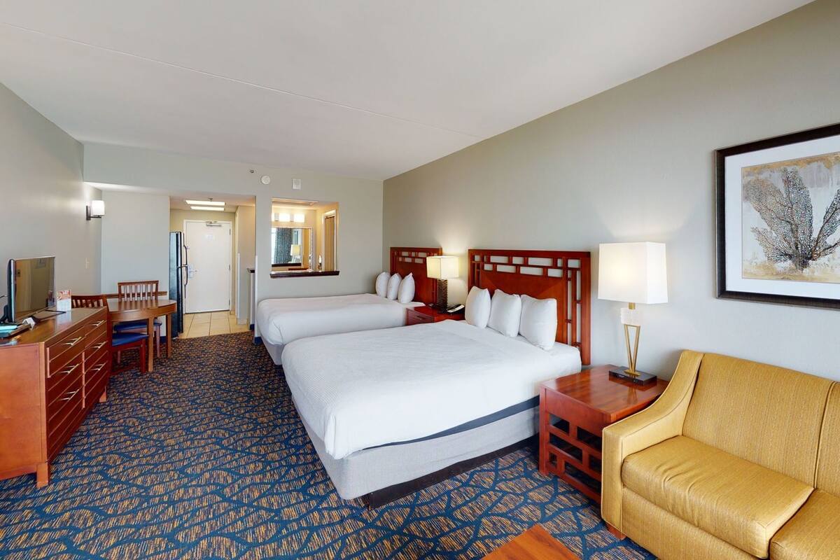 A hotel room with two beds, a desk, a chair, a sofa, and a framed picture on the wall.
