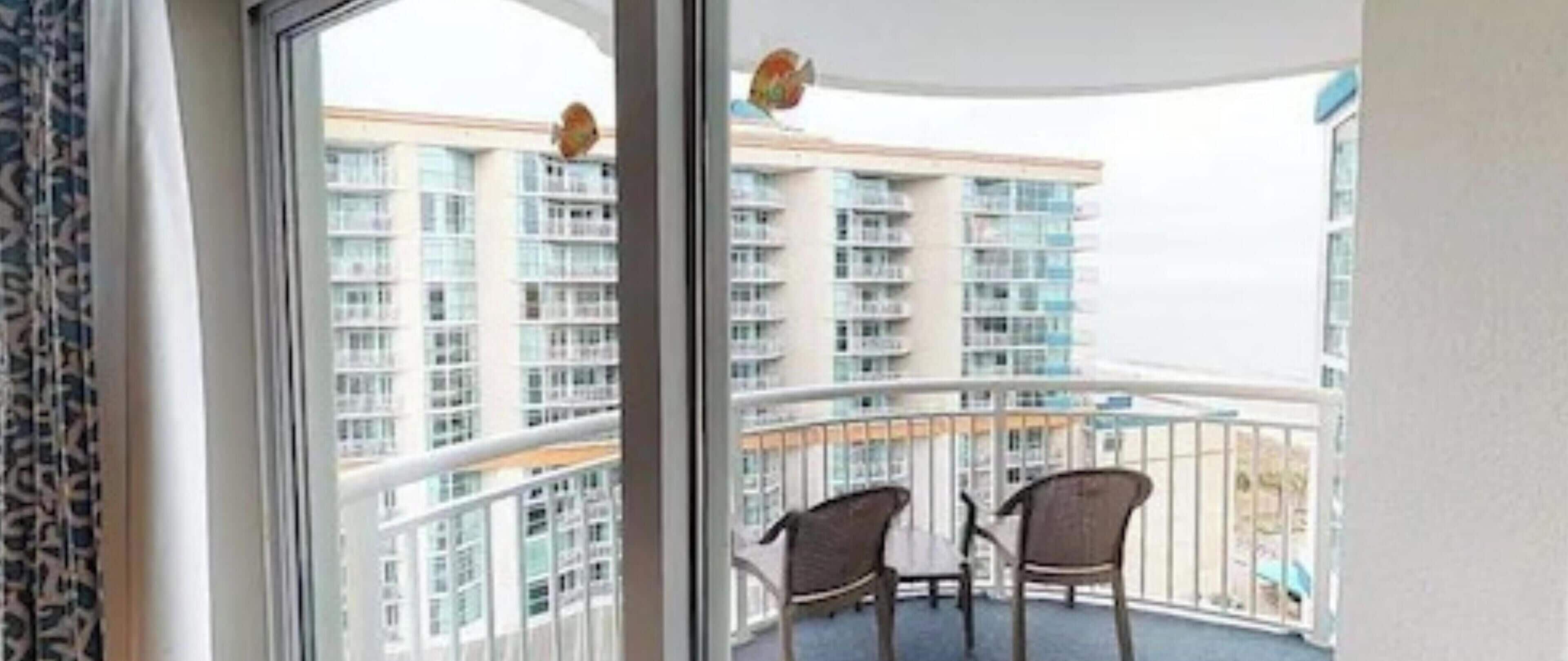 A balcony with two wicker chairs and a table, overlooking a high-rise building with multiple balconies.