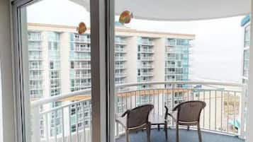Un balcón con dos sillones de mimbre y una mesa, con vista a un edificio de gran altura con múltiples balcones.