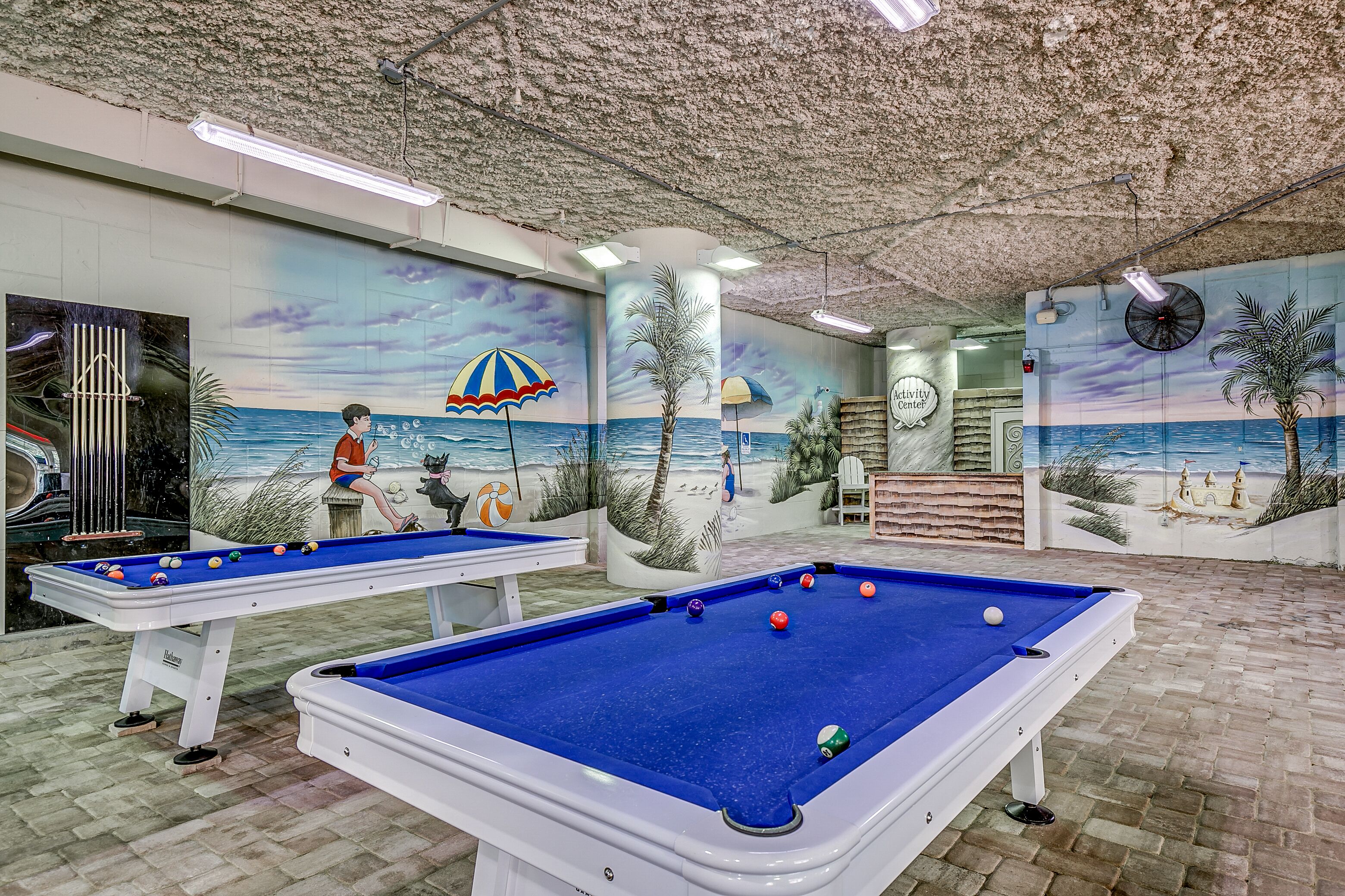 A pool table with a beach mural, another pool table, and a ceiling with a textured finish.