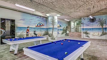 A pool table with a beach mural, another pool table, and a ceiling with a textured finish.