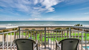 Un balcon avec deux chaises, une piscine et une vue sur la plage et l’océan.