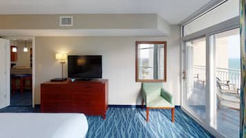 A hotel room with a bed, a TV on a wooden dresser, a chair, and a balcony with a view of the ocean.
