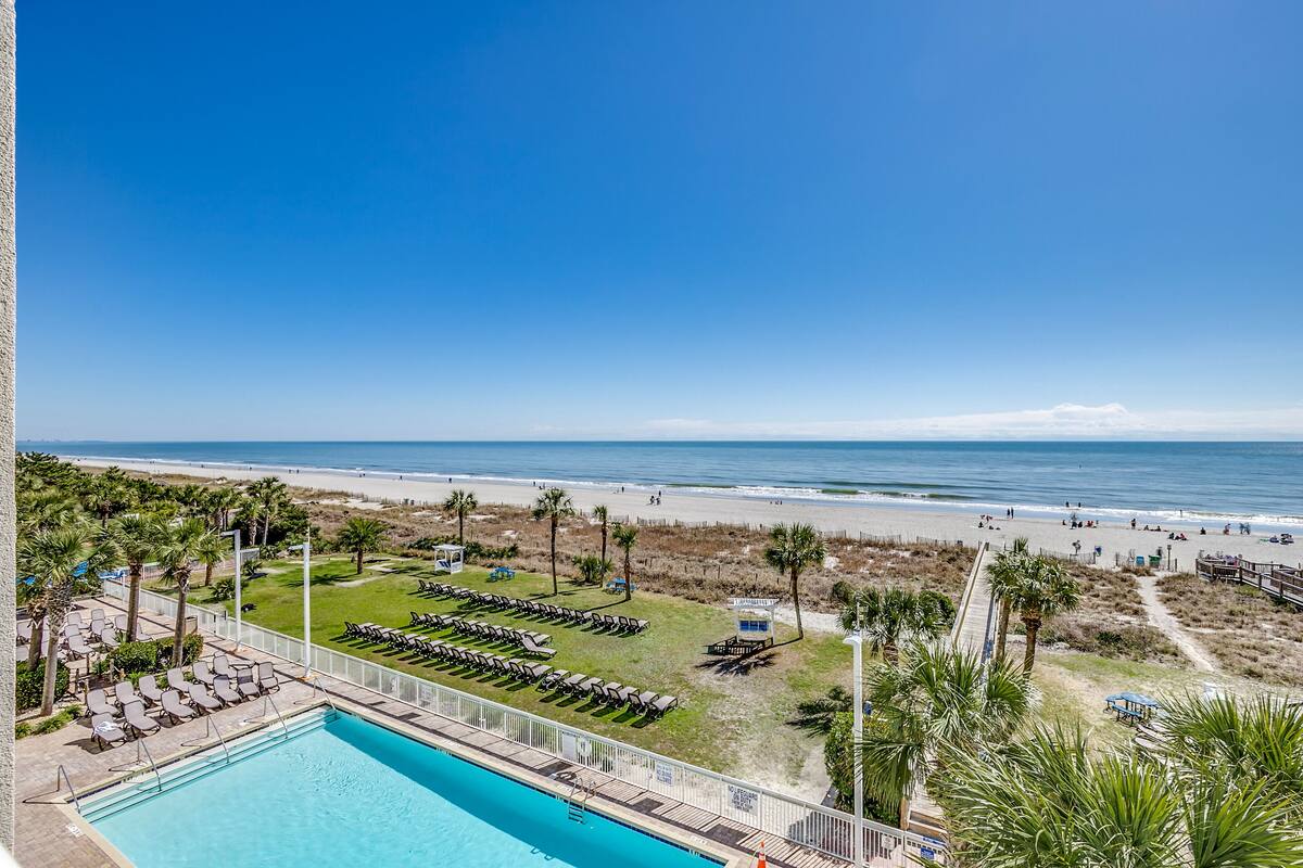 A pool area with lounge chairs and a view of the beach.