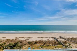 Une vue sur la plage, avec un ciel dégagé, une plage de sable et un espace piscine équipé de chaises longues.