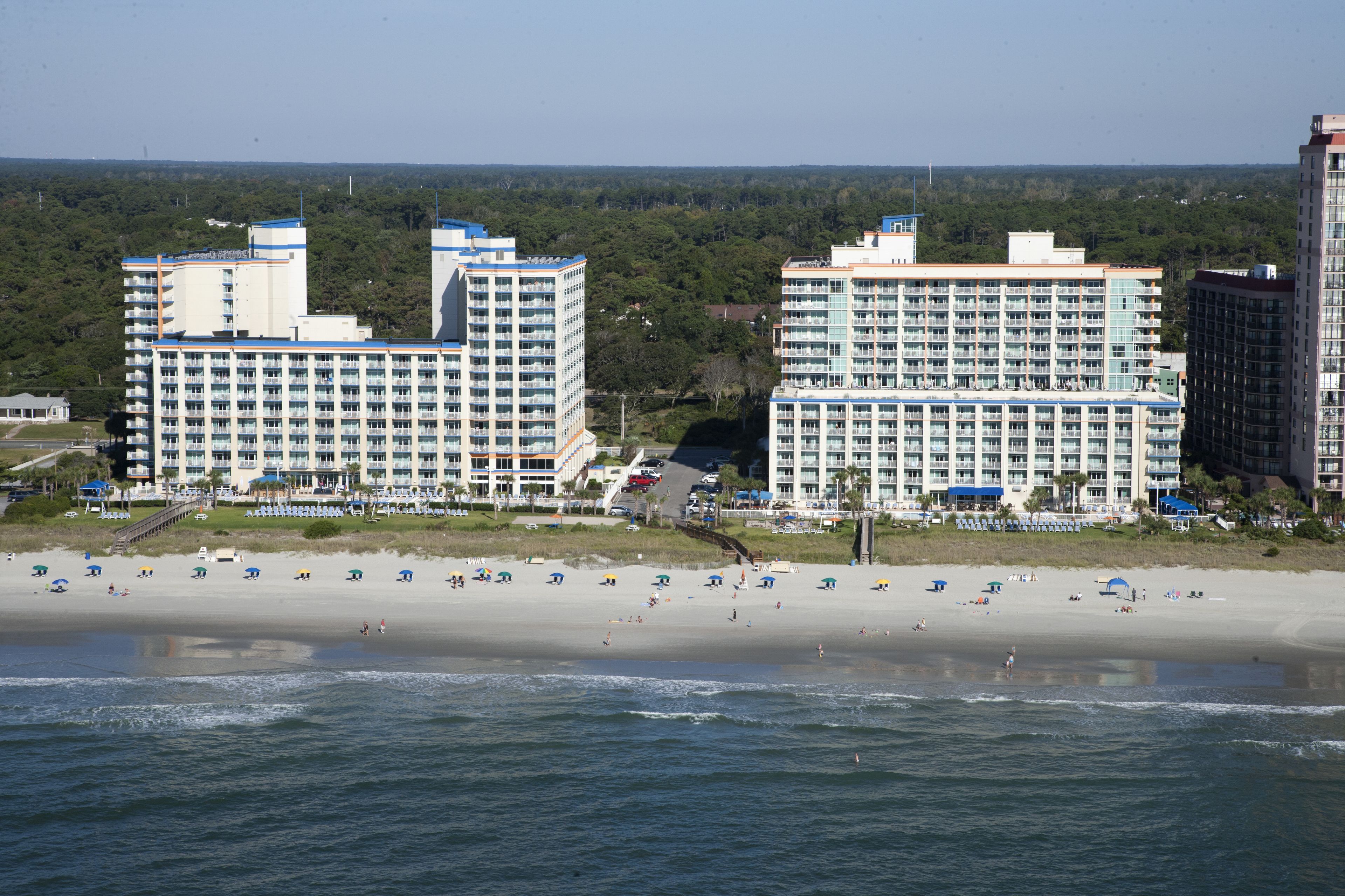 A beachfront hotel with multiple high-rise buildings, a sandy beach, and a view of the ocean.