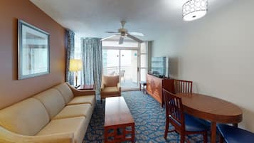 A hotel room with a sofa, a wooden table, a TV, and a balcony with a view.