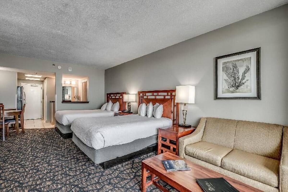 A hotel room with two beds, a sofa, a desk, and a chair.