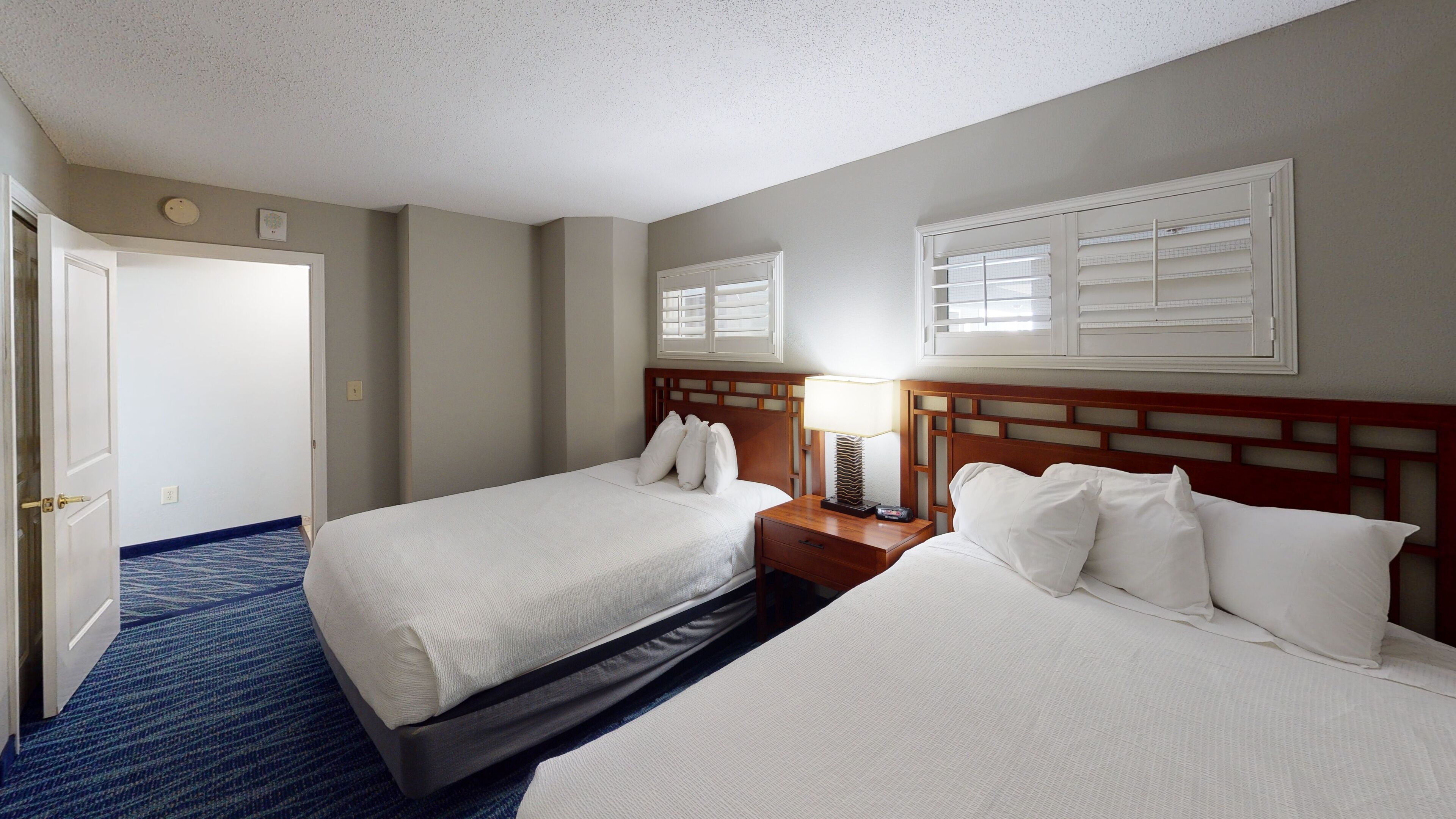 Une chambre d’hôtel avec deux lits, une table de chevet, une lampe et une fenêtre avec des stores.