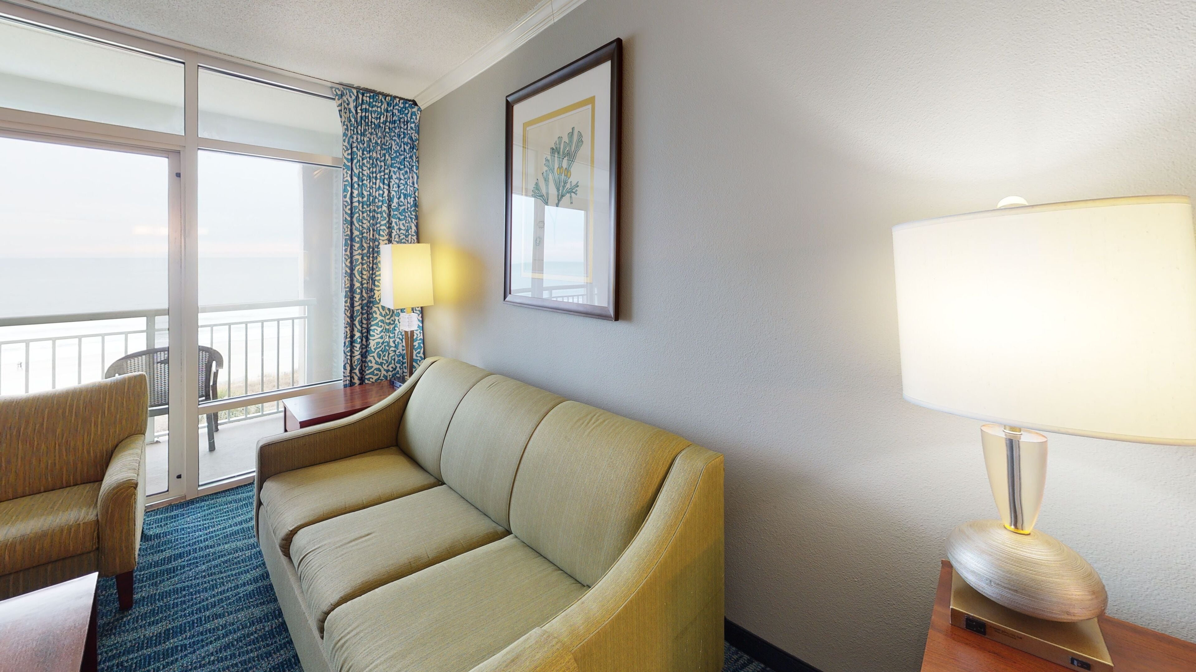 Une chambre d’hôtel avec un canapé, une table, une lampe et un tableau encadré au mur.