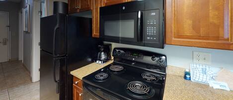 A kitchen with a black refrigerator, a microwave, a stove, and wooden cabinets.