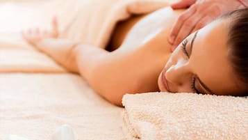 A person receiving a massage on a bed with a towel and stones.