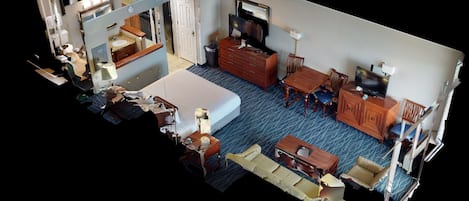 A hotel room with a bed, a desk, a chair, a TV, a dresser, and a bathroom.