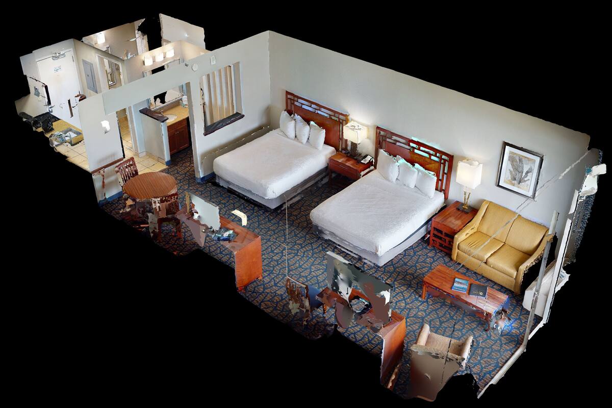A hotel room with two beds, a sofa, a dining table, and a small kitchen area.