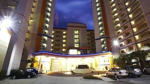 Un hôtel à plusieurs étages, doté d’une entrée principale, d’un parking et entouré d’immeubles de grande hauteur.
