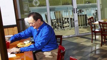 Un homme déjeune dans un restaurant qui offre une vue sur l’espace piscine.