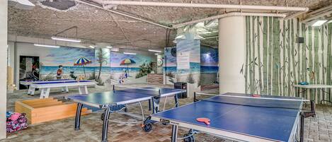 Une pièce équipée de tables de ping-pong, ornée d’une fresque murale et dont les murs sont décorés de motifs en bambou.