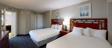 A hotel room with two beds, a wooden headboard, a bedside table with a lamp, a framed picture on the wall, and a patterned carpet.