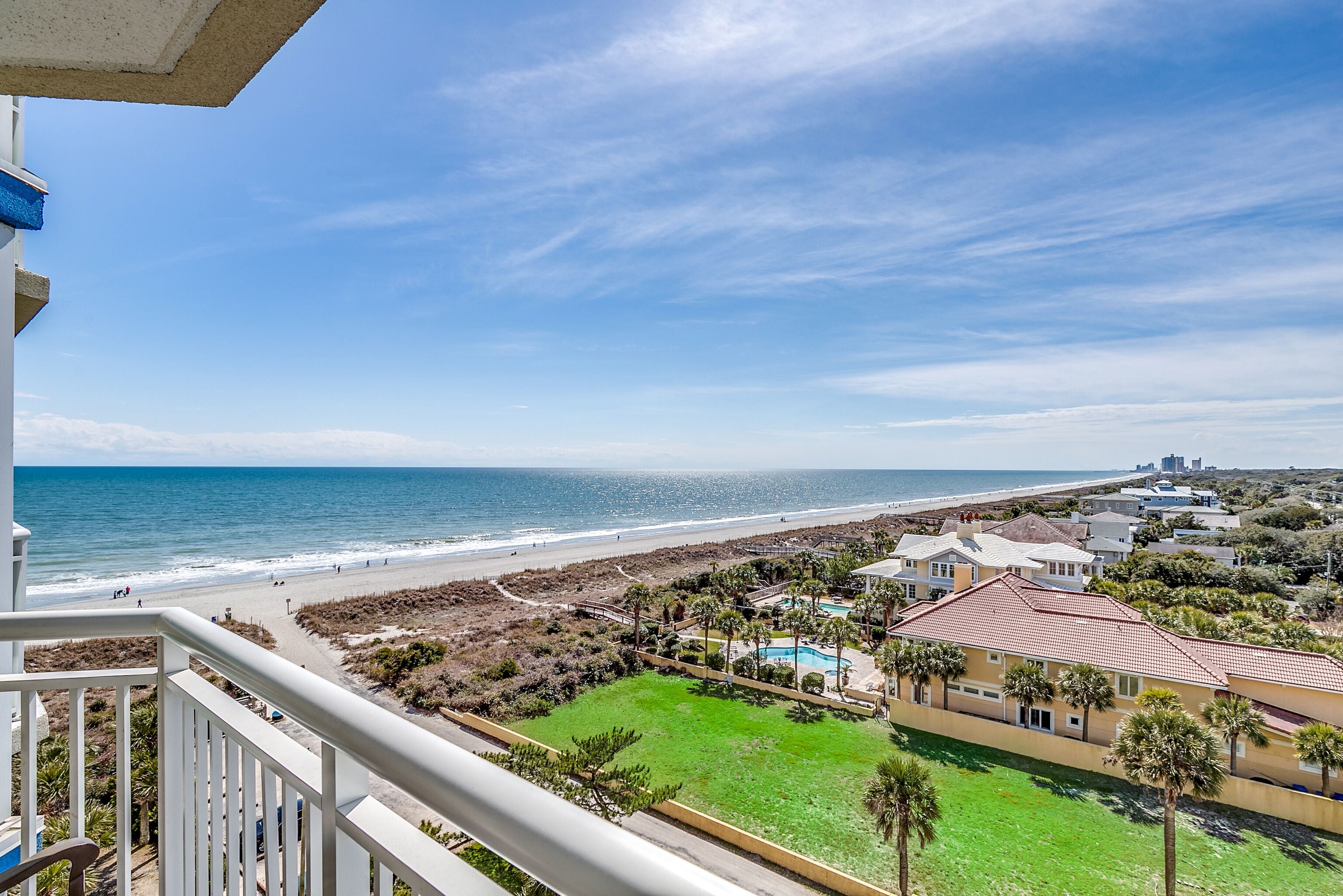 A beachfront property with a pool, a tennis court, and a view of the ocean.
