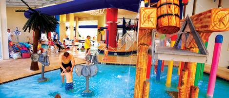 A water play area with slides and a pool, surrounded by colorful structures and a covered seating area.