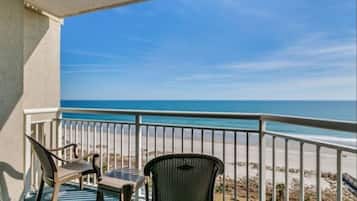 A balcony with two chairs and a table, overlooking a beach with a clear sky.