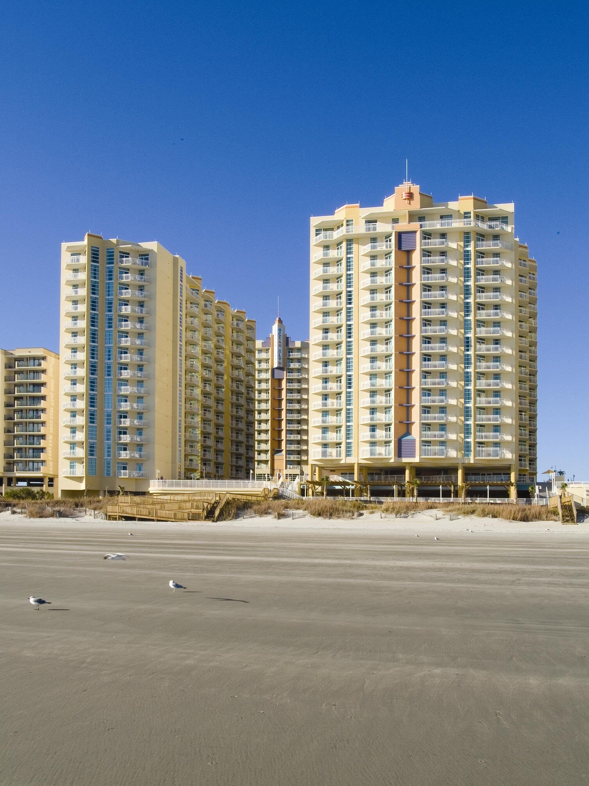 A beachfront hotel with multiple high-rise buildings, a boardwalk, and a sandy beach.