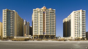 A beachfront high-rise hotel with multiple balconies, a sandy beach in the foreground, and clear blue skies. - Club Wyndham Ocean Boulevard (North Myrtle Beach)