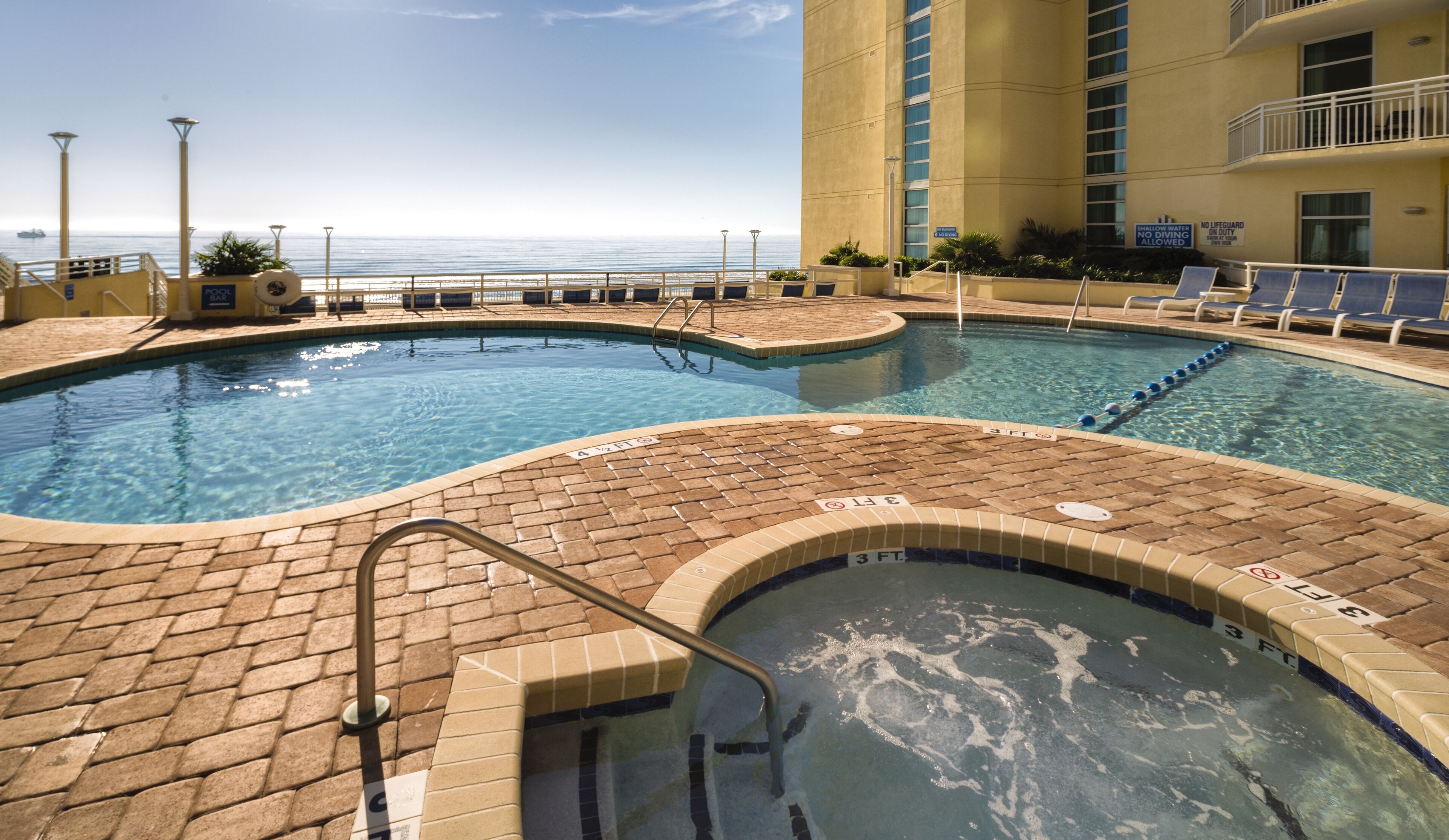 Zona de piscina con vista al océano, un jacuzzi y sillones de descanso.
