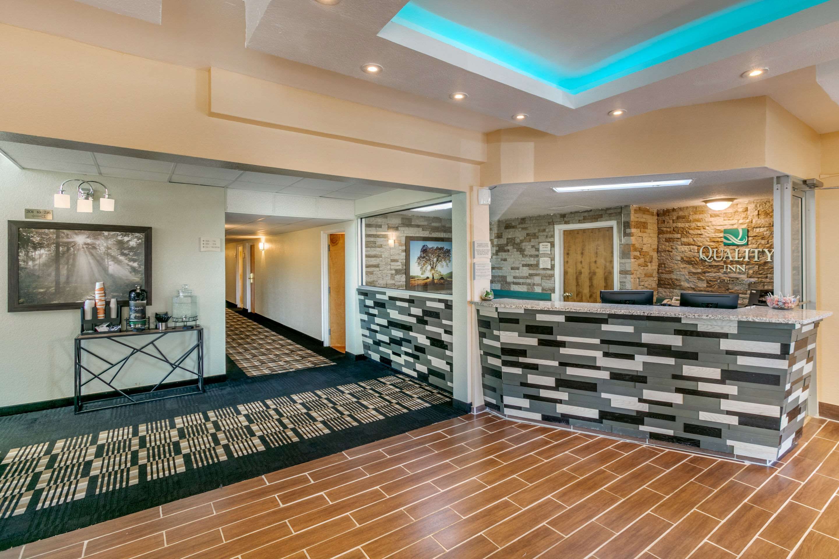 A hotel reception area with a modern design, including a reception desk with a stone facade and a staircase leading to another floor.