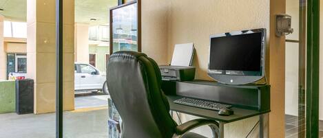 A hotel room with a desk, computer, and a view of the street outside.