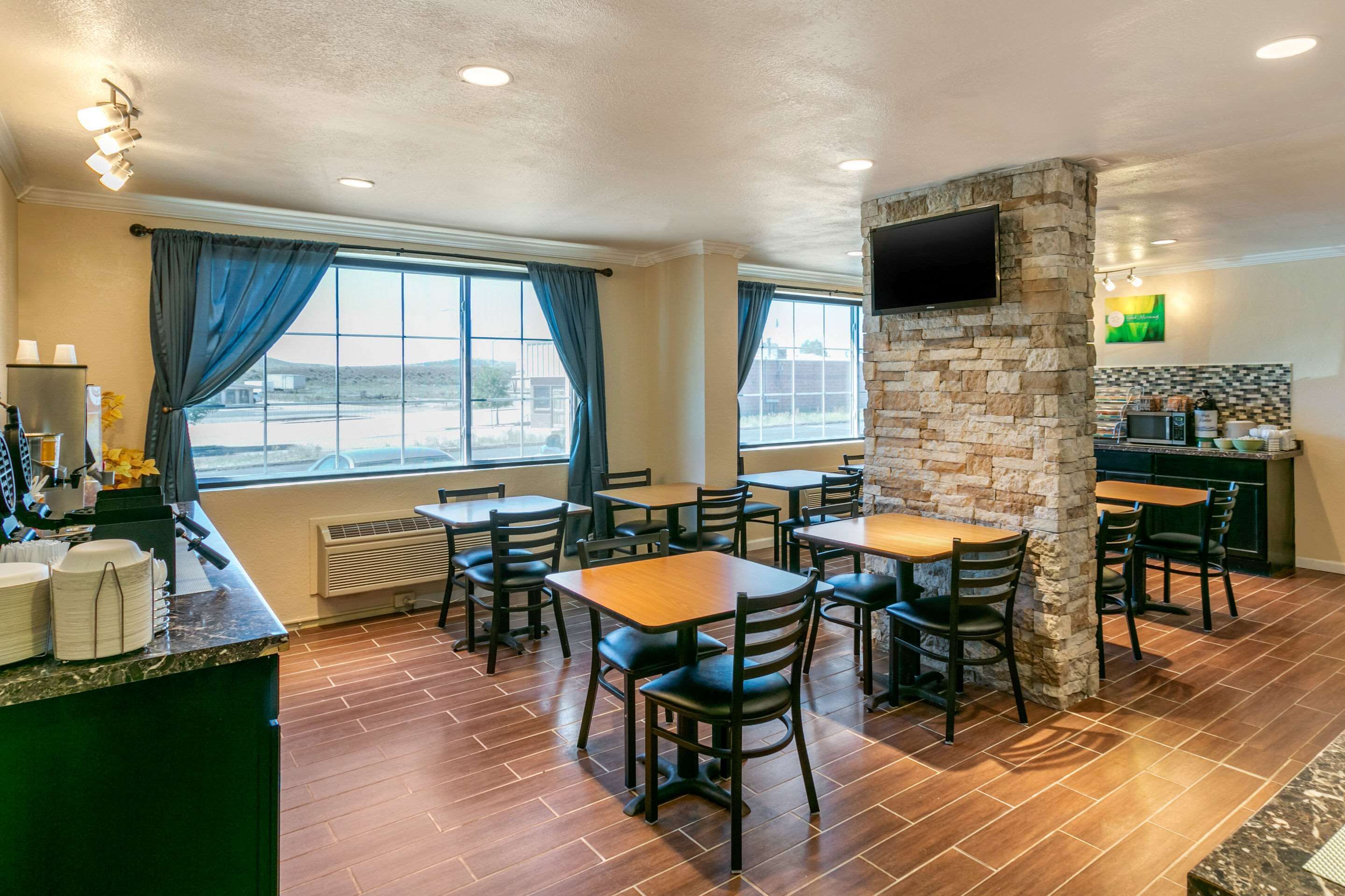 A restaurant with multiple tables and chairs, a stone pillar, a flat-screen TV mounted on the wall, and a view of the outside through large windows.