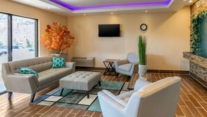 A modern living room with a sofa, ottoman, and chairs, a flat-screen TV, a clock, and a large window with a view of a parking lot. - Quality Inn Rawlins I-80 (Rawlins)