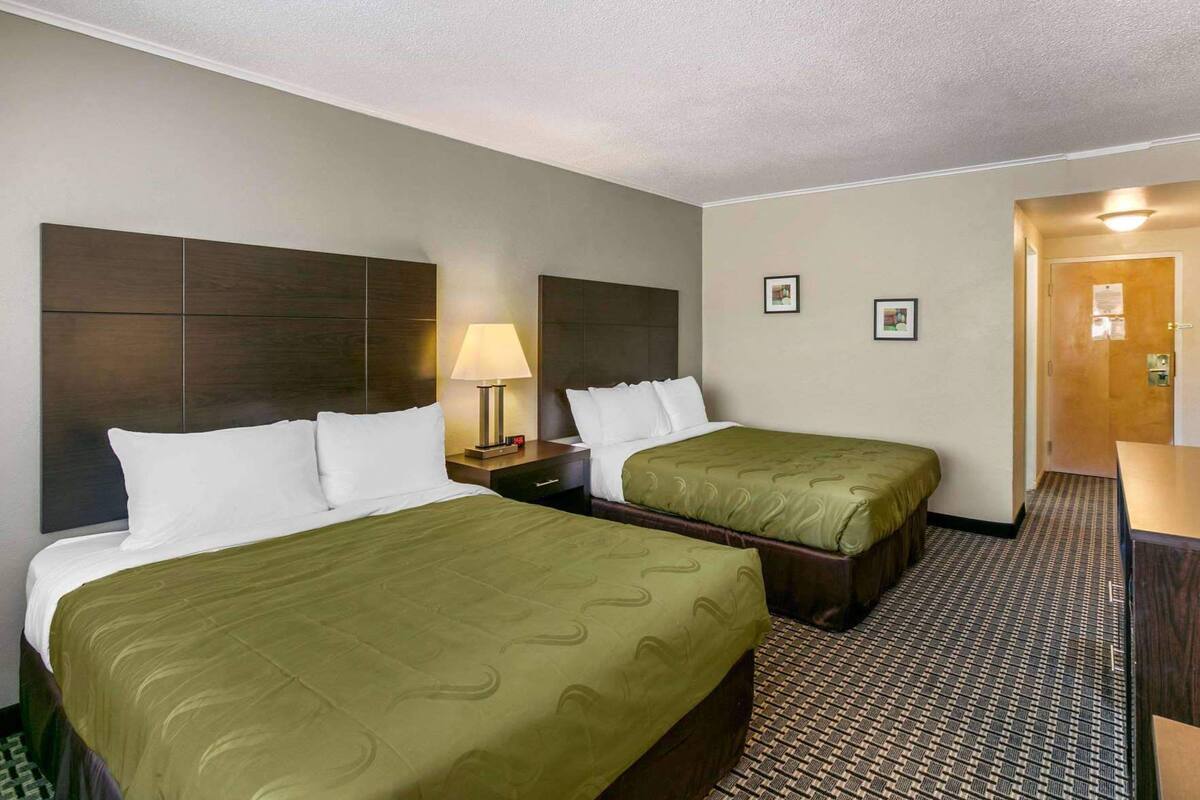 Una habitación de hotel con dos camas, una mesita de noche, una lámpara y una puerta.