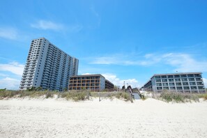 A beachfront hotel with multiple high-rise buildings, a sandy beach in the foreground, and a clear blue sky. - Myrtle Beach Resort by Beach Vacations (Myrtle Beach)