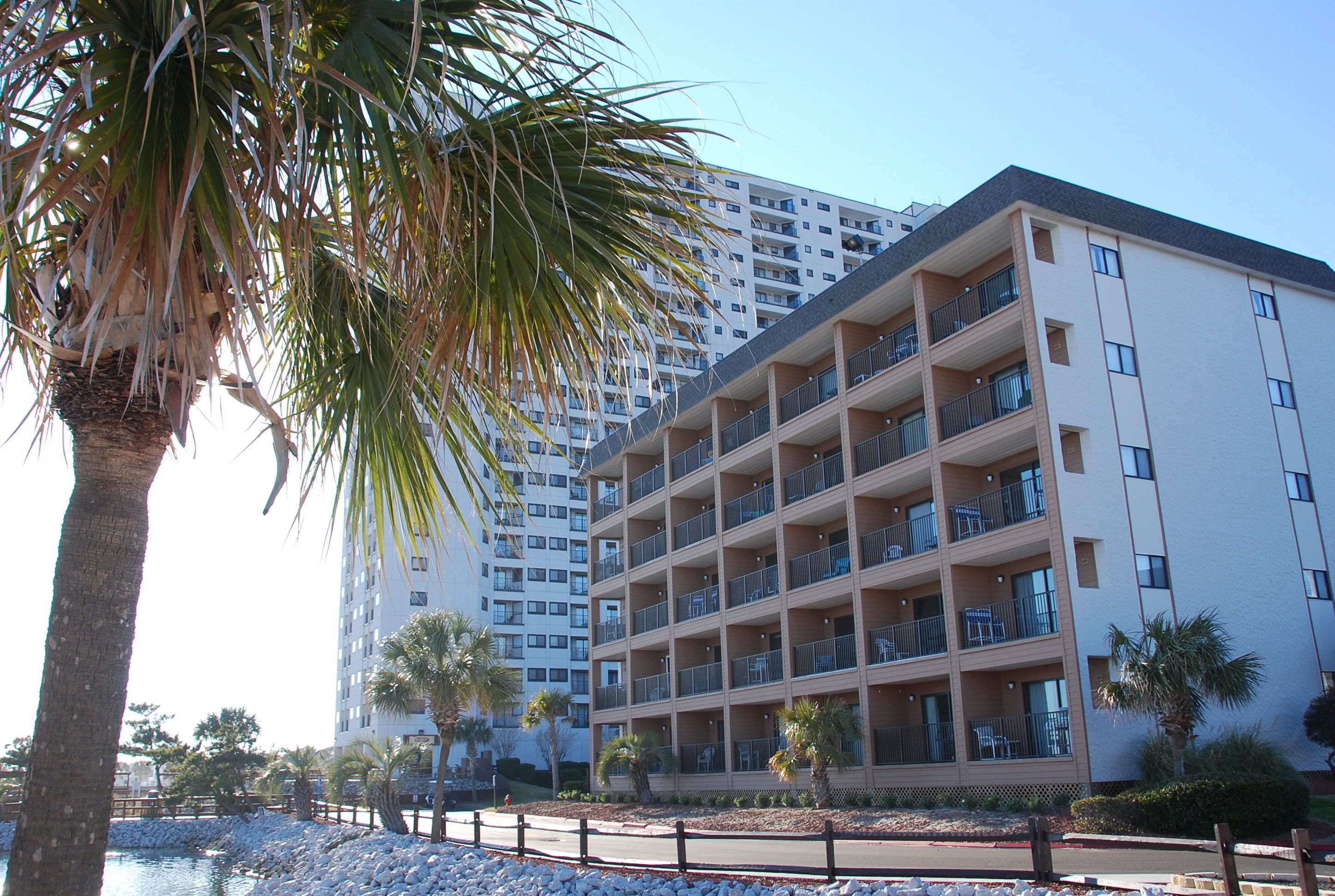 A multi-story hotel with balconies, a pool area, and palm trees.
