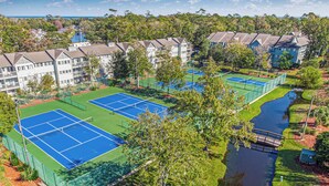 Ett tenniscenter med flera banor, omgivet av bostadshus och en liten vattendekoration.