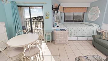 A room with a dining table, chairs, a bed, a sofa, and a view through a sliding door.