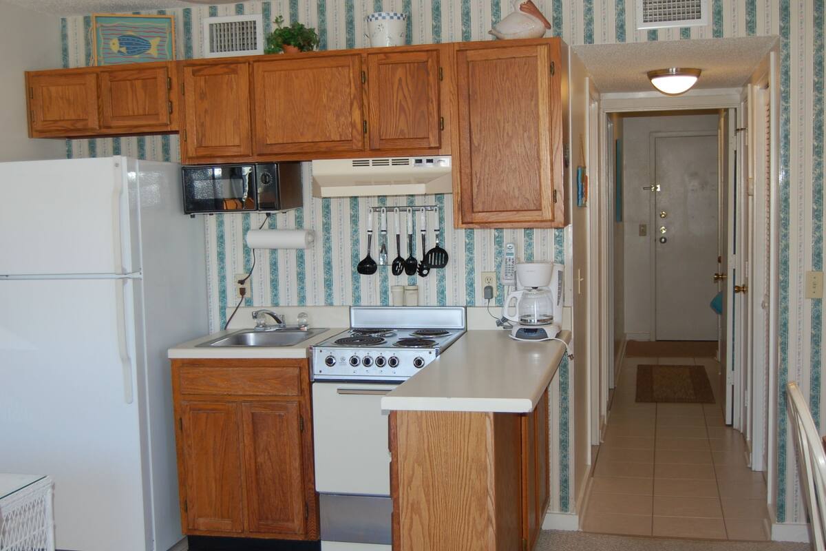 A compact kitchen with wooden cabinets, a stove, a microwave, and a coffee maker.