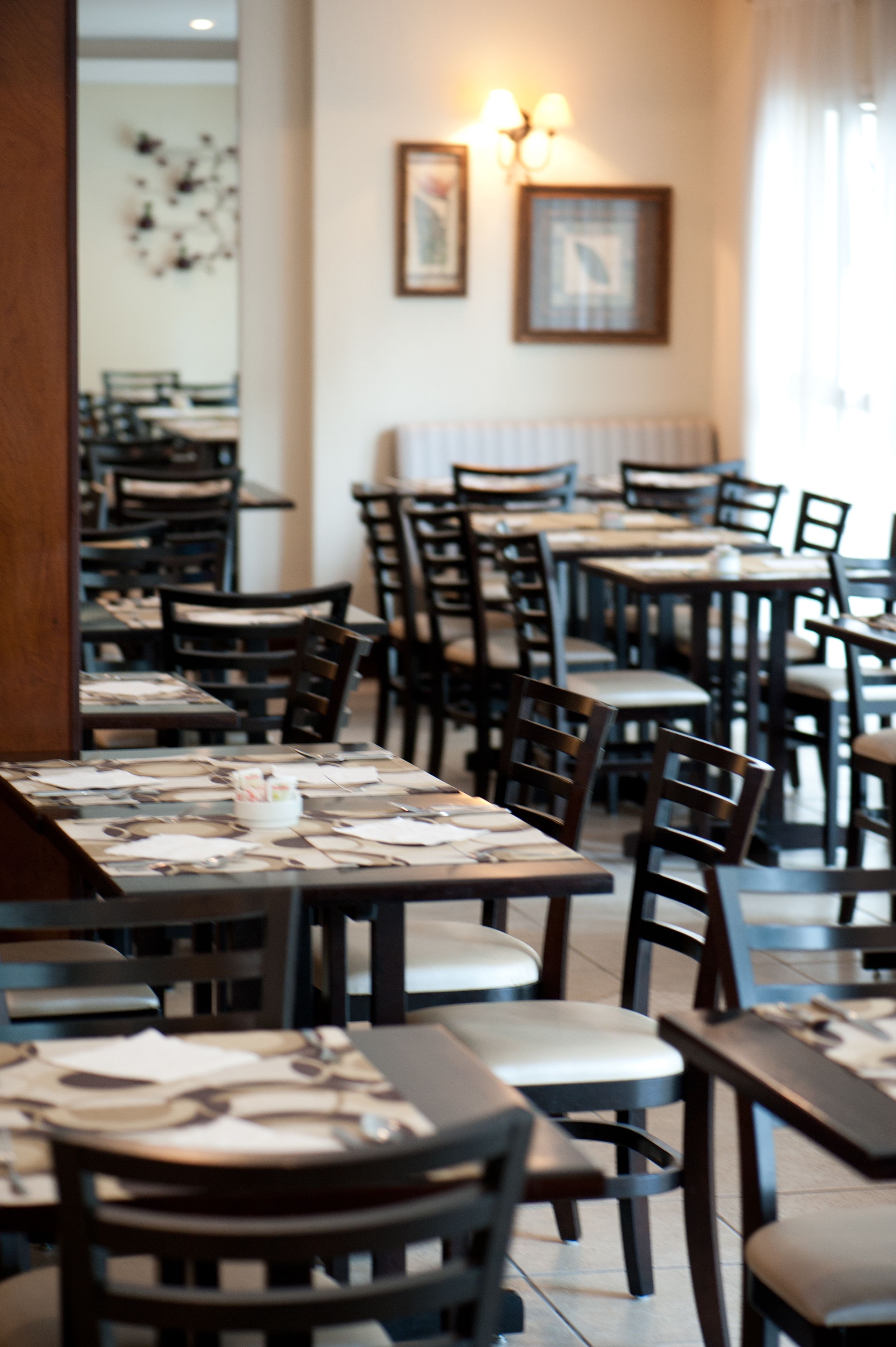 A restaurant interior with multiple tables and chairs, a mirror on the left, and framed pictures on the wall.