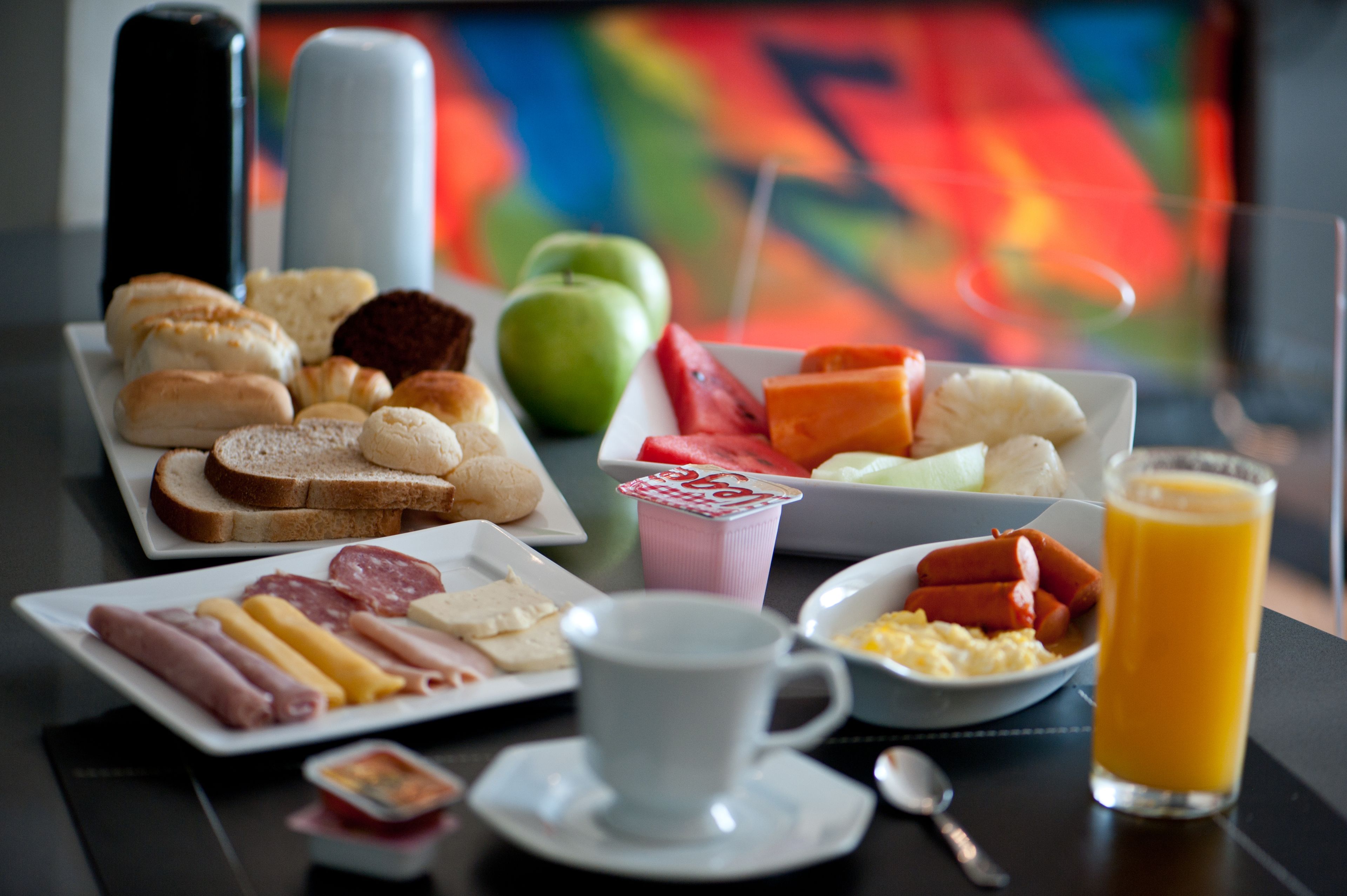 Una mesa de desayuno con diversos alimentos, como pan, salchichas, huevos y un vaso de jugo de naranja.