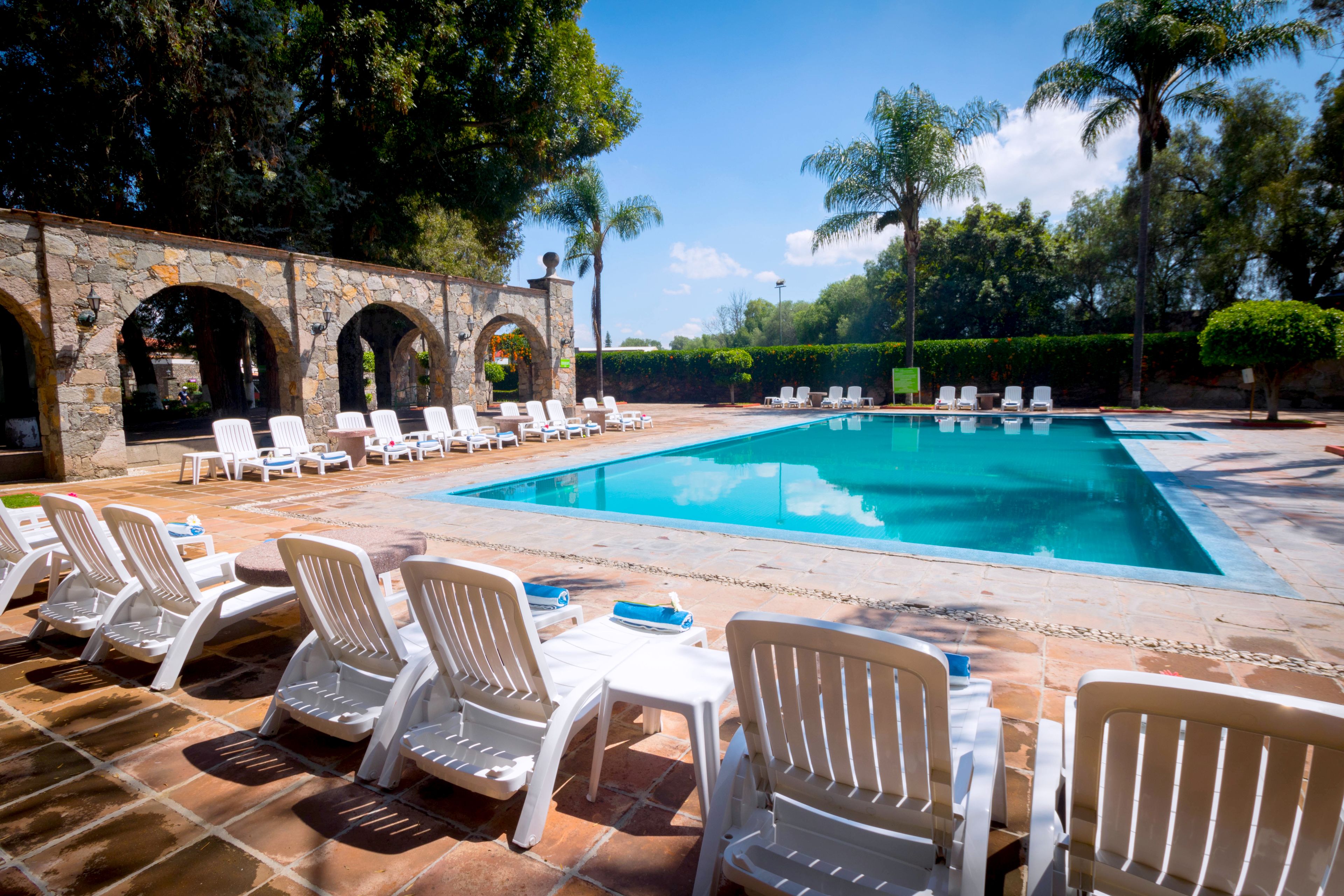 Un área de piscina con sillas reclinables blancas y un arco de piedra.