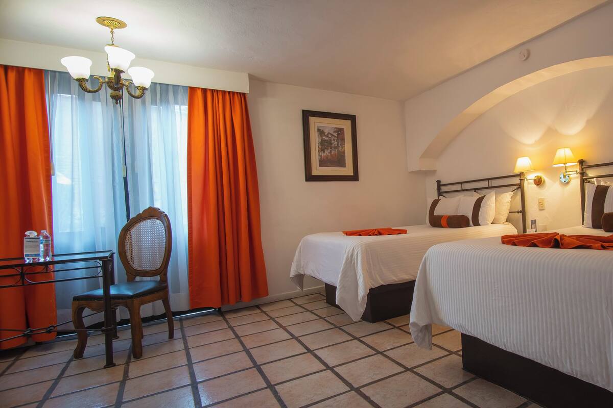 Habitación de hotel con dos camas, un escritorio con silla y un candelabro.