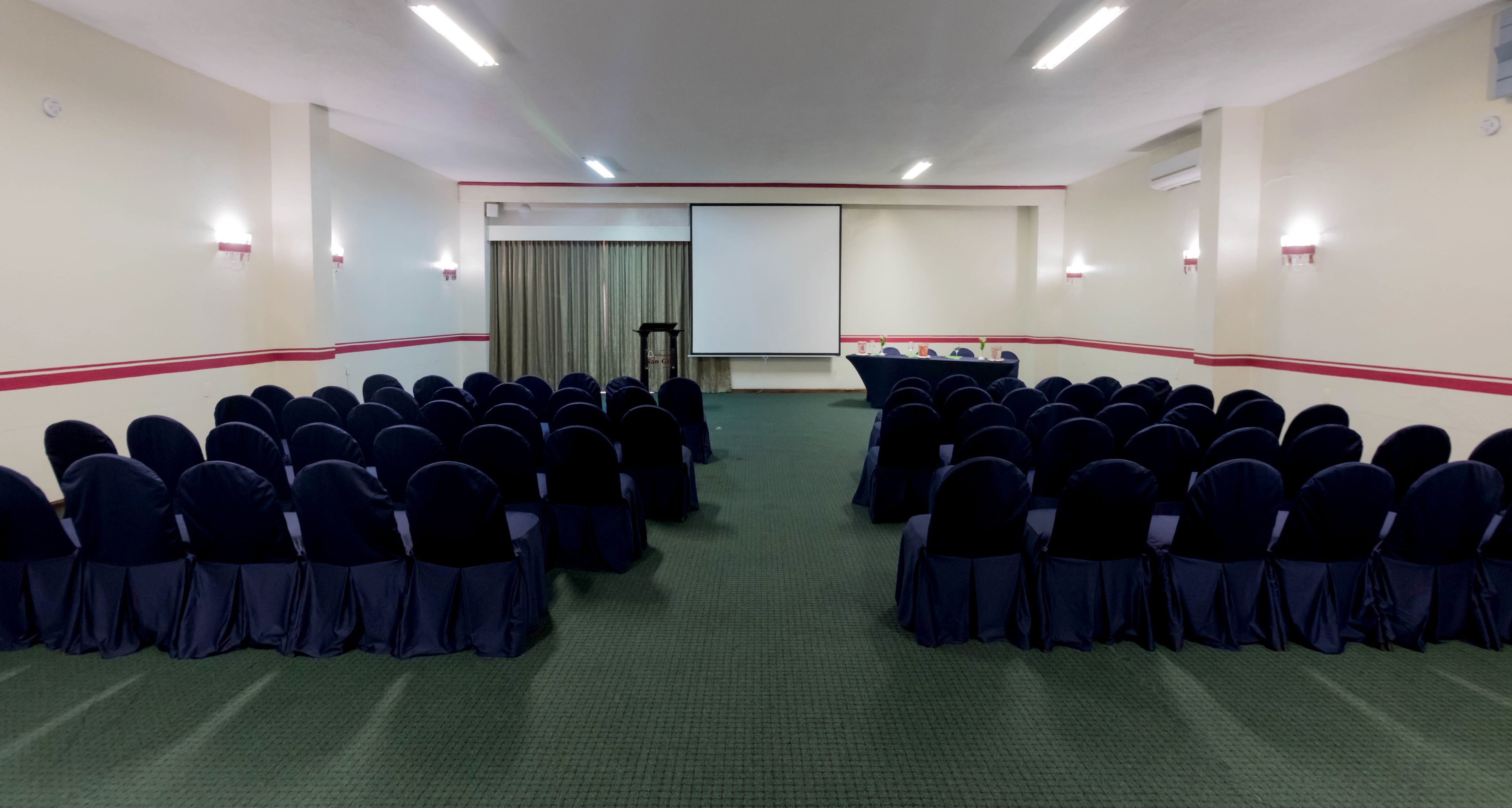 A conference room with rows of chairs, a projector screen, and a podium.
