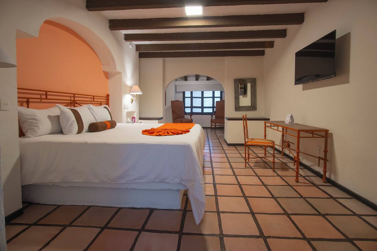 Un dormitorio con una cama grande, un escritorio, una silla, un arco de entrada y un televisor montado en la pared.