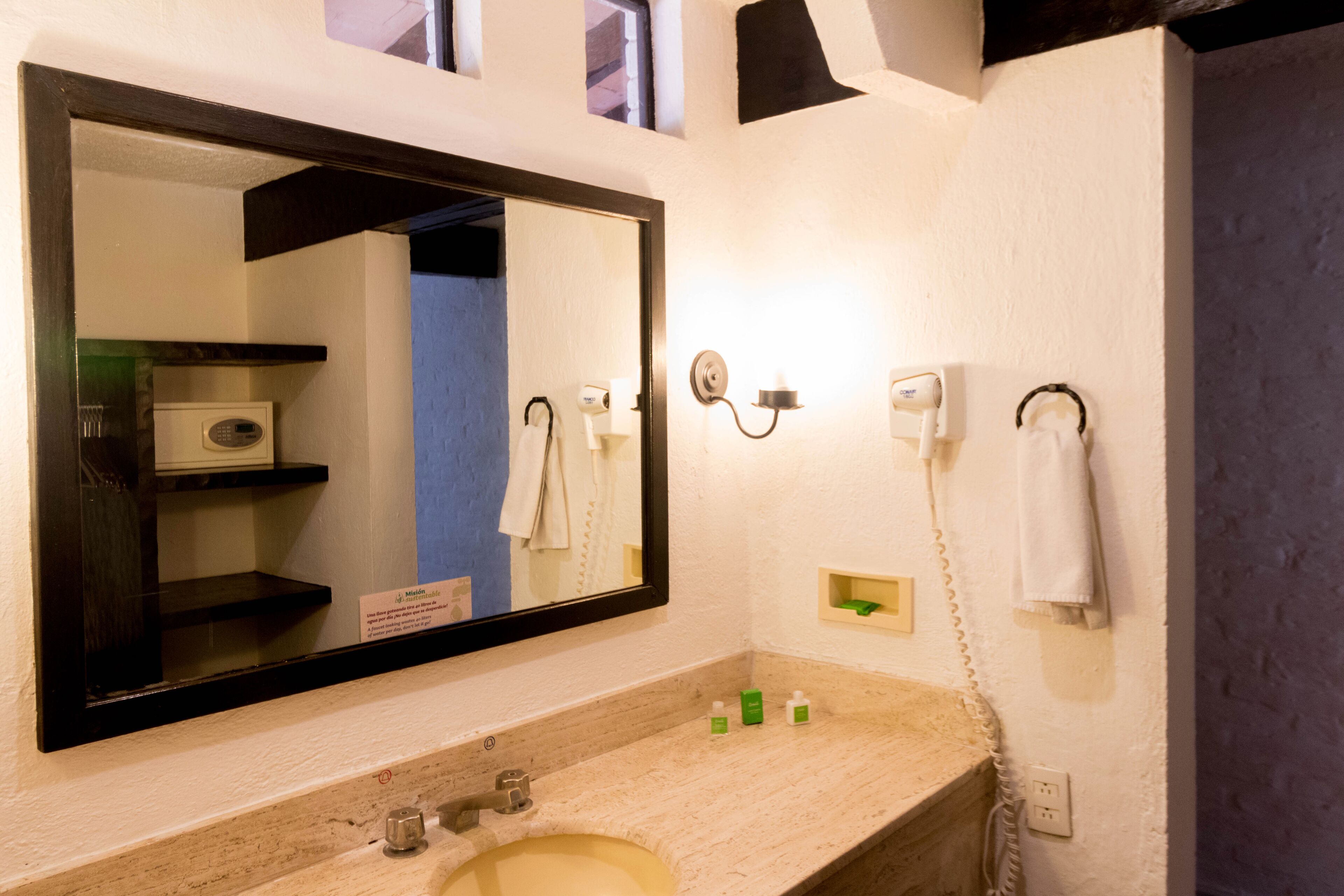 A bathroom with a large mirror, a sink, a hairdryer, and a towel rack.