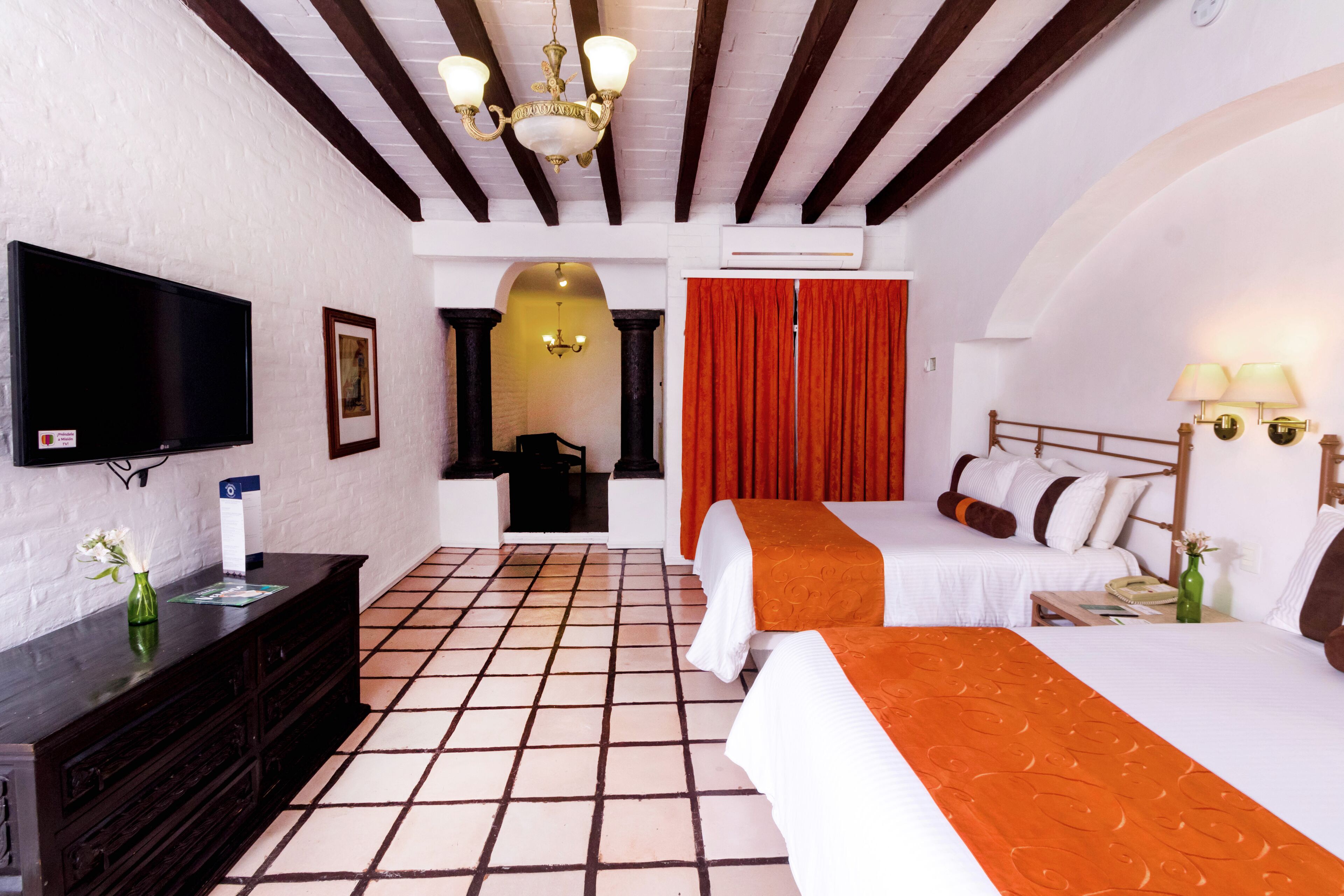 A hotel room with two beds, a TV, a dresser, and a tiled floor.