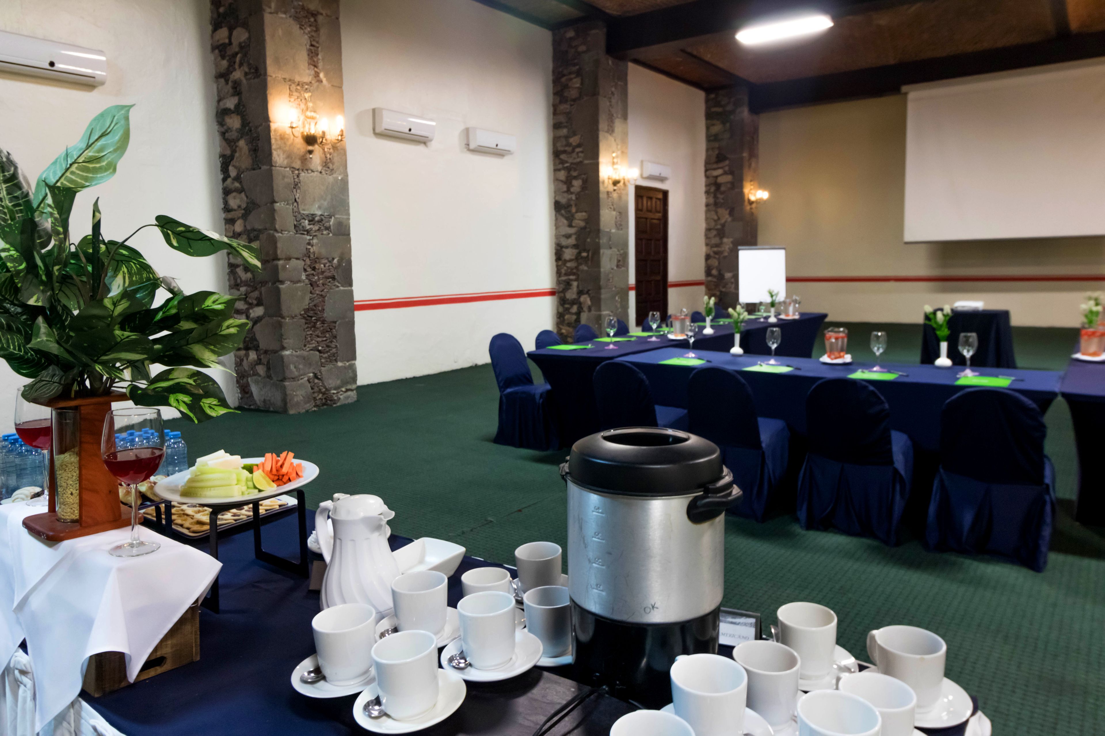 A conference room with a long table set for a meeting, surrounded by chairs, and a coffee pot on the table.