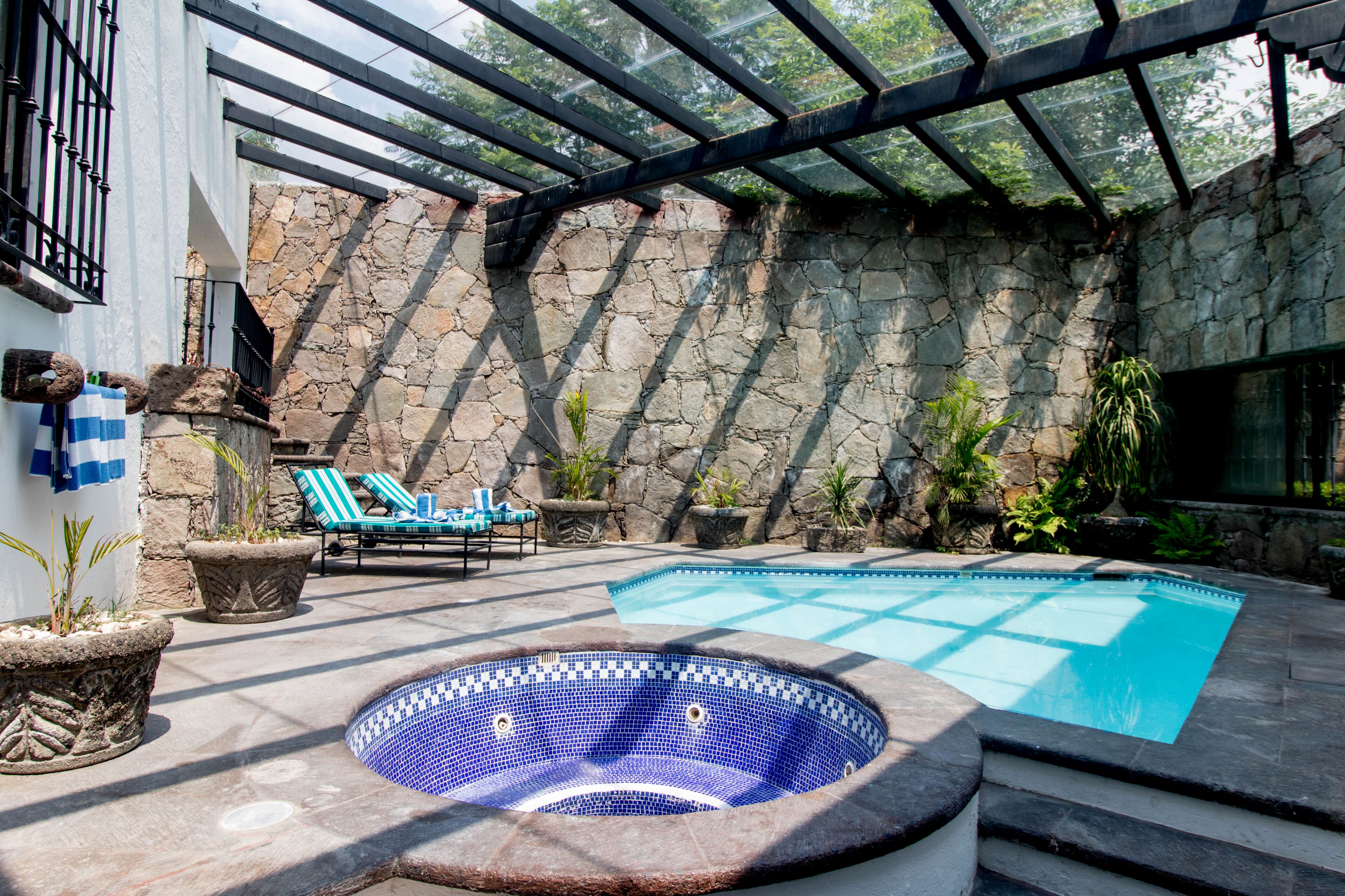 A pool area with a hot tub, lounge chairs, and stone walls.