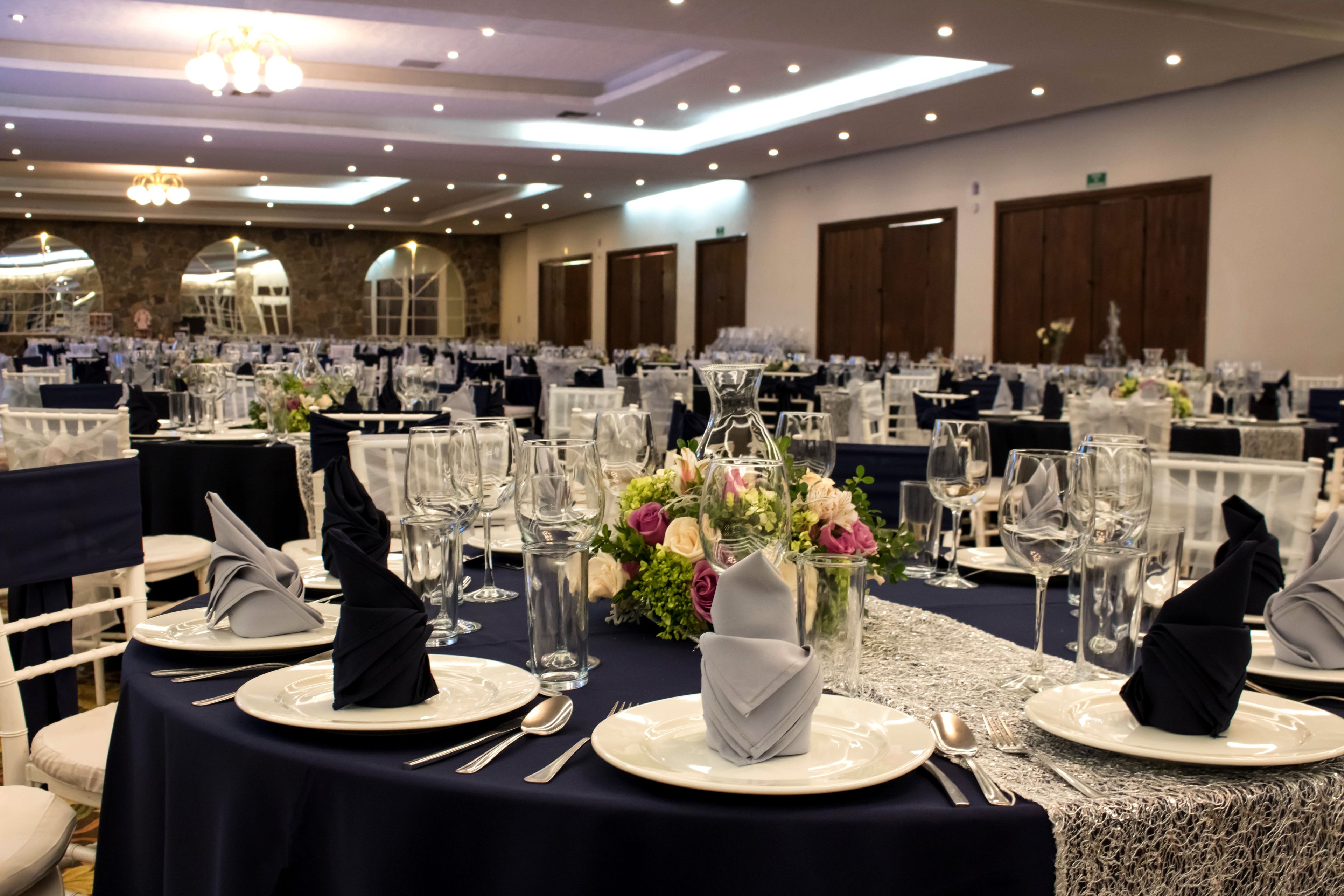 A banquet hall with round tables set for a formal event, featuring white tablecloths, neatly folded napkins, and clear glassware.